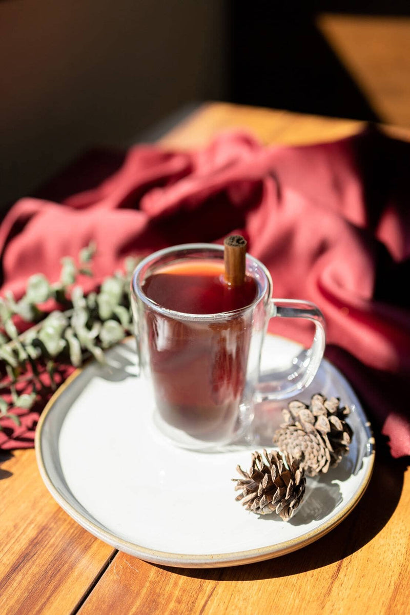 Clear glass mug filled with brown drink and cinnamon stick surrounded by earthen materials