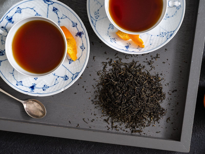 Two cups of tea with bergamot orange rinds on the saucer and loose tea leaves on a tray