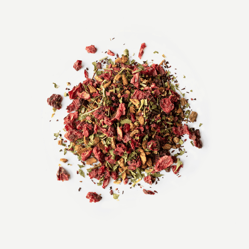 A pile of Rishi Tea & Botanicals loose herbal tea blend with dried hibiscus, adaptogenic schisandra berry, green leaves, and brown root pieces is shown on a white background.